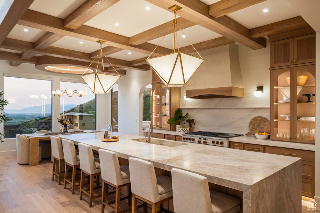 Kitchen with custom exhaust hood, range, light wood finished floors, tasteful backsplash, and beam ceiling