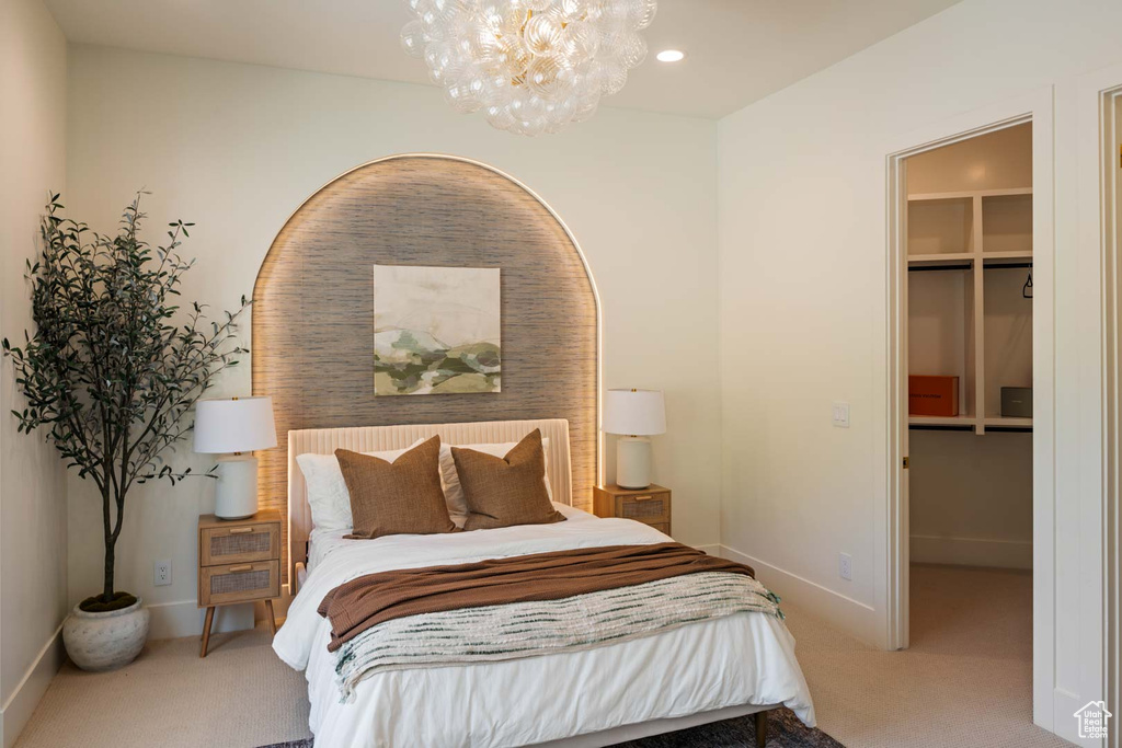 Carpeted bedroom featuring a walk in closet, a chandelier, baseboards, and a closet