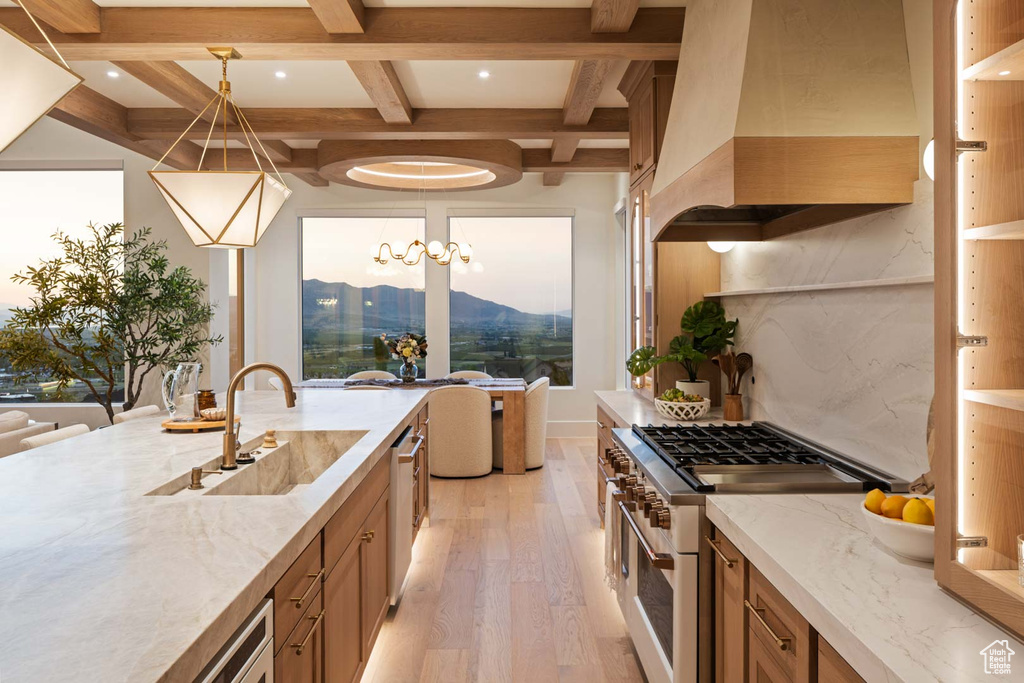 Kitchen with custom exhaust hood, double oven range, a sink, light wood-style floors, and coffered ceiling