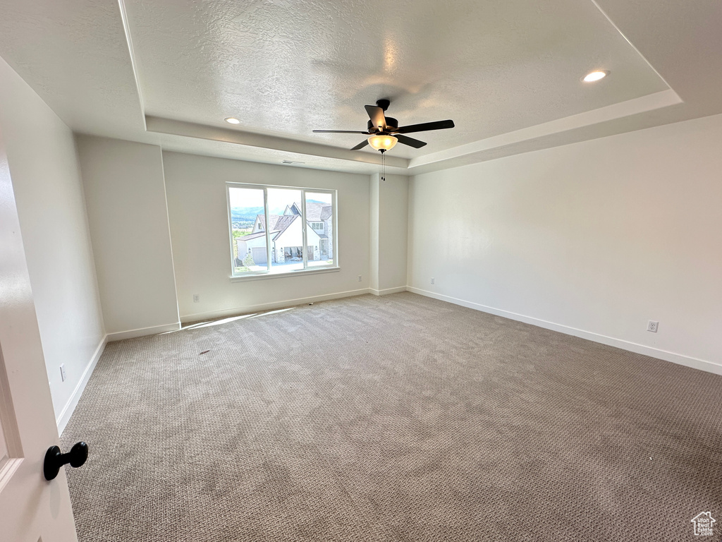 Empty room featuring a tray ceiling, a ceiling fan, carpet floors, recessed lighting, and a textured ceiling