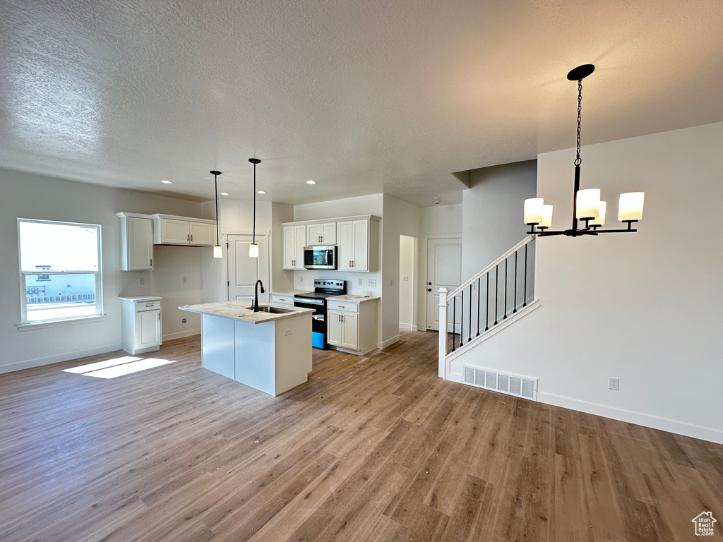 Kitchen with stainless steel appliances, light wood finished floors, an island with sink, baseboards, and white cabinets