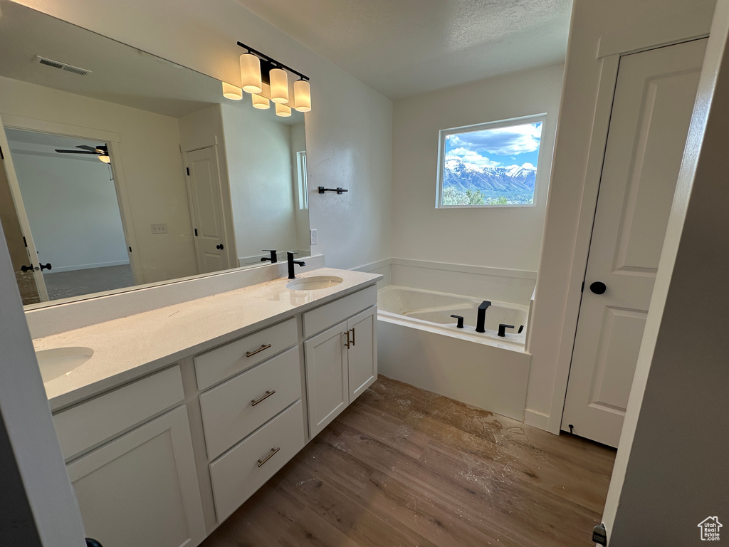 Full bathroom with wood finished floors, double vanity, a garden tub, and a ceiling fan