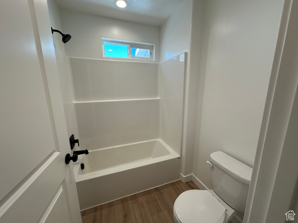 Full bathroom with toilet, wood finished floors, and shower / washtub combination