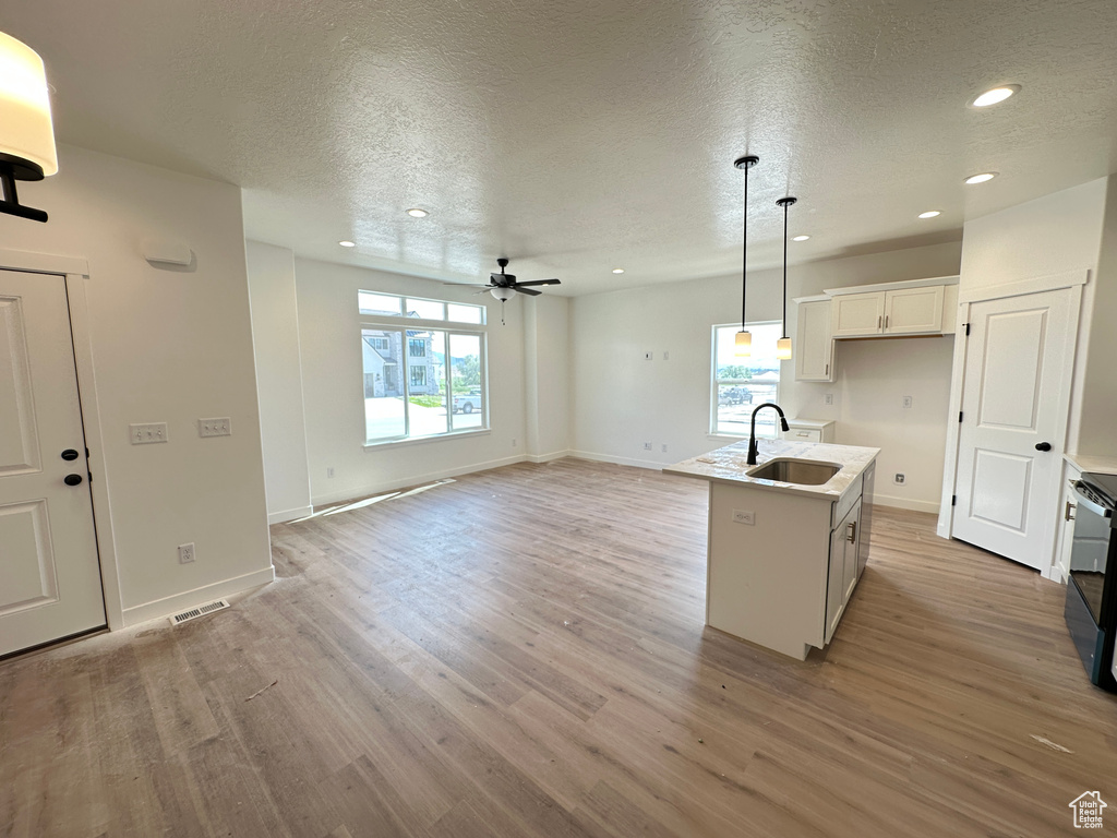 Kitchen with a sink, a textured ceiling, light wood-type flooring, recessed lighting, and hanging light fixtures