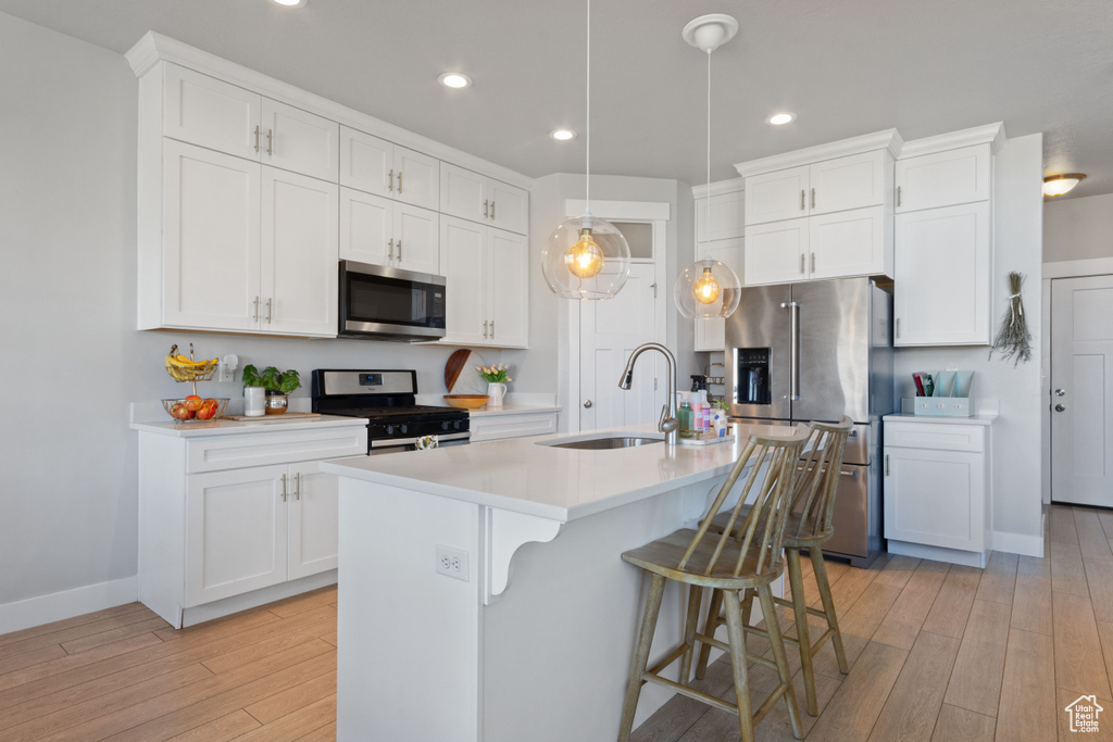 Kitchen featuring appliances with stainless steel finishes, a sink, light wood finished floors, light countertops, and a kitchen bar