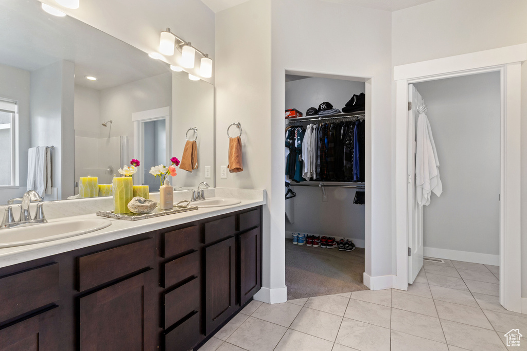 Full bath with tile patterned floors, double vanity, a walk in closet, a shower, and baseboards