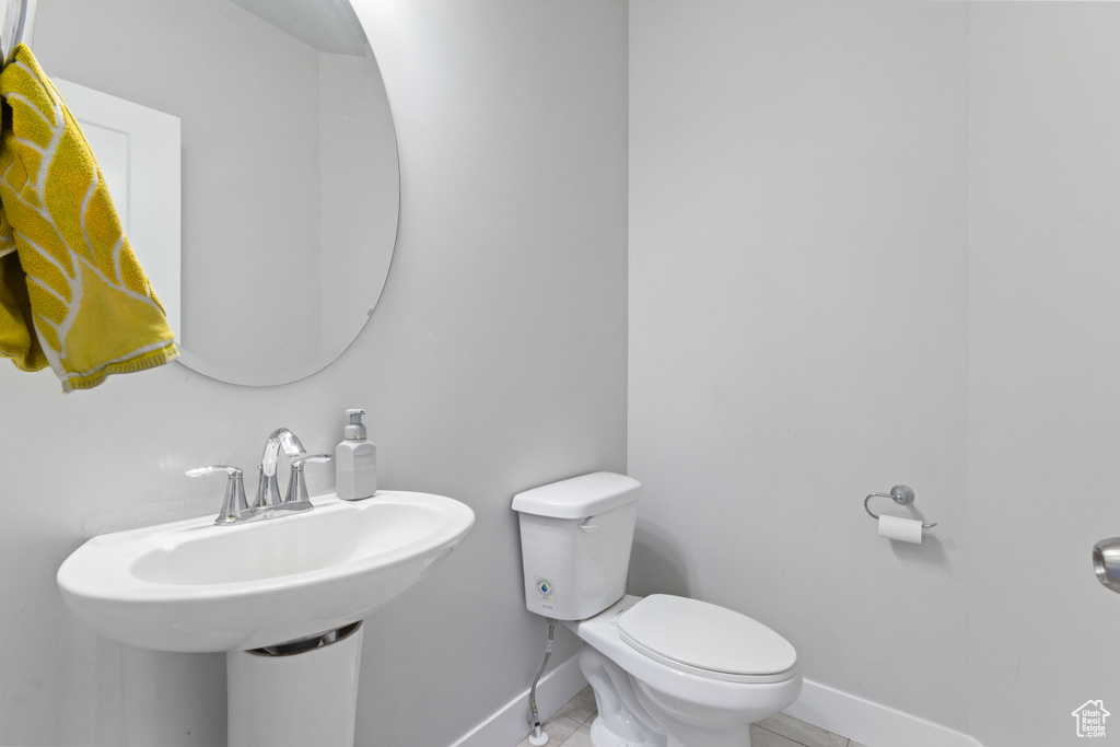 Half bath with baseboards, toilet, tile patterned flooring, and a sink