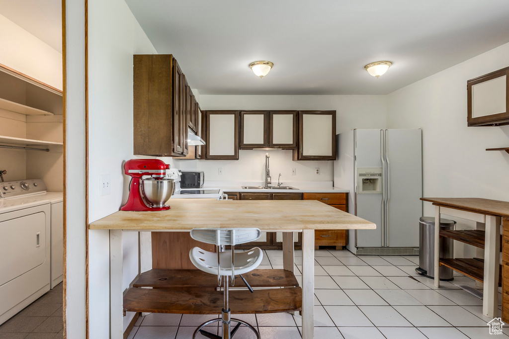 Kitchen featuring white fridge with ice dispenser, washing machine and clothes dryer, a sink, light countertops, and a peninsula