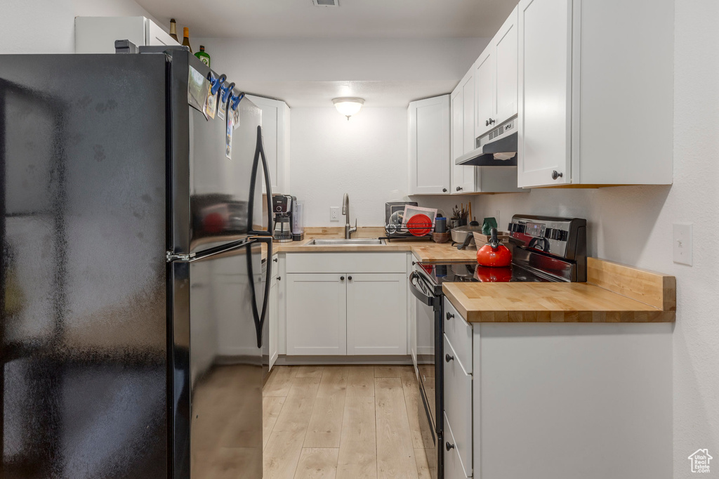 Kitchen featuring stainless steel electric stove, freestanding refrigerator, a sink, under cabinet range hood, and wooden counters