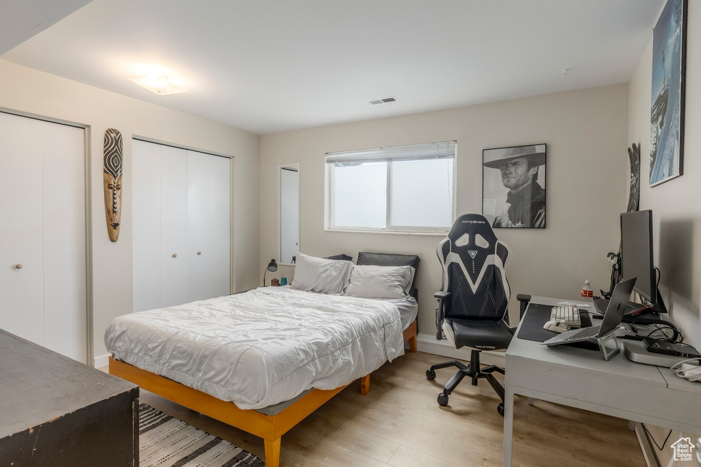 Bedroom with light wood-style floors, a desk, and multiple closets