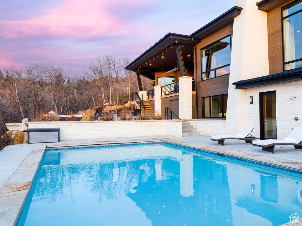 Pool at dusk featuring stairway, an outdoor pool, and a patio area