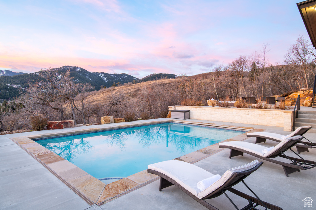Pool at dusk with a mountain view and a patio