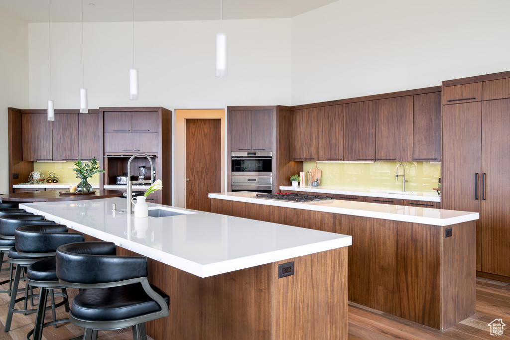 Kitchen with a large island with sink, modern cabinets, a sink, a high ceiling, and tasteful backsplash