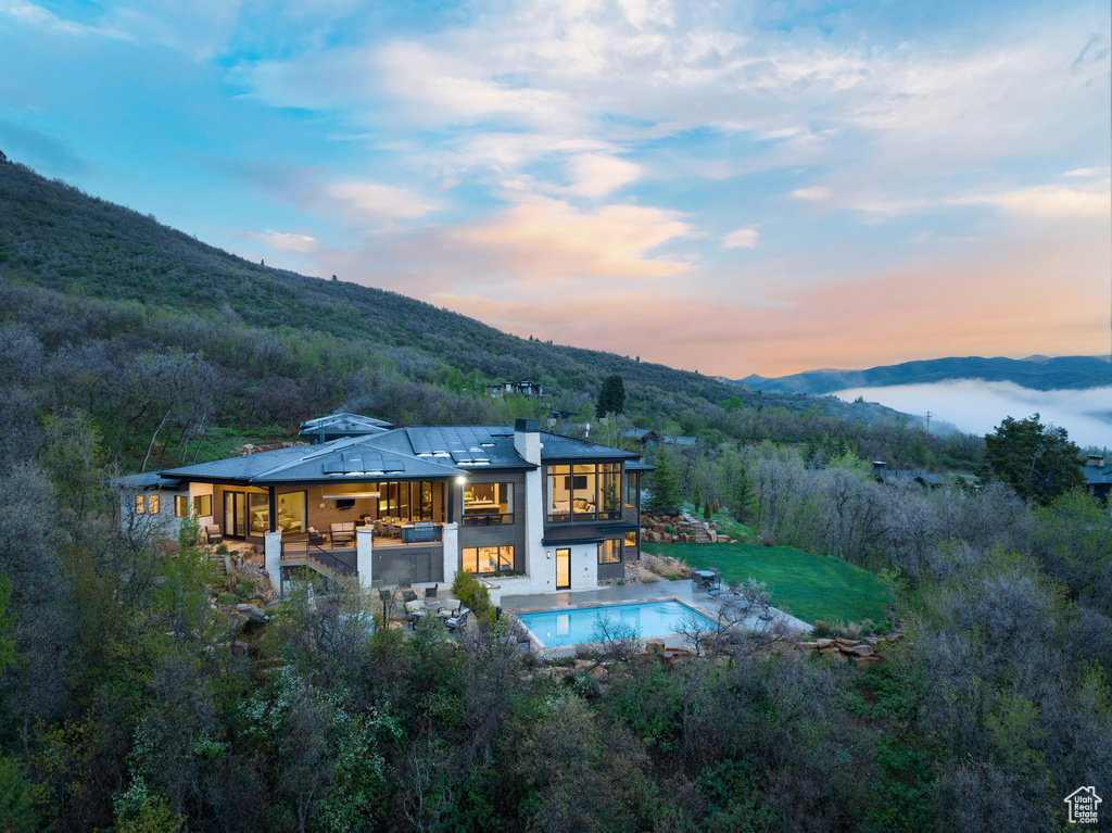 Back of property with a mountain view, an outdoor pool, a balcony, a patio, and a view of trees