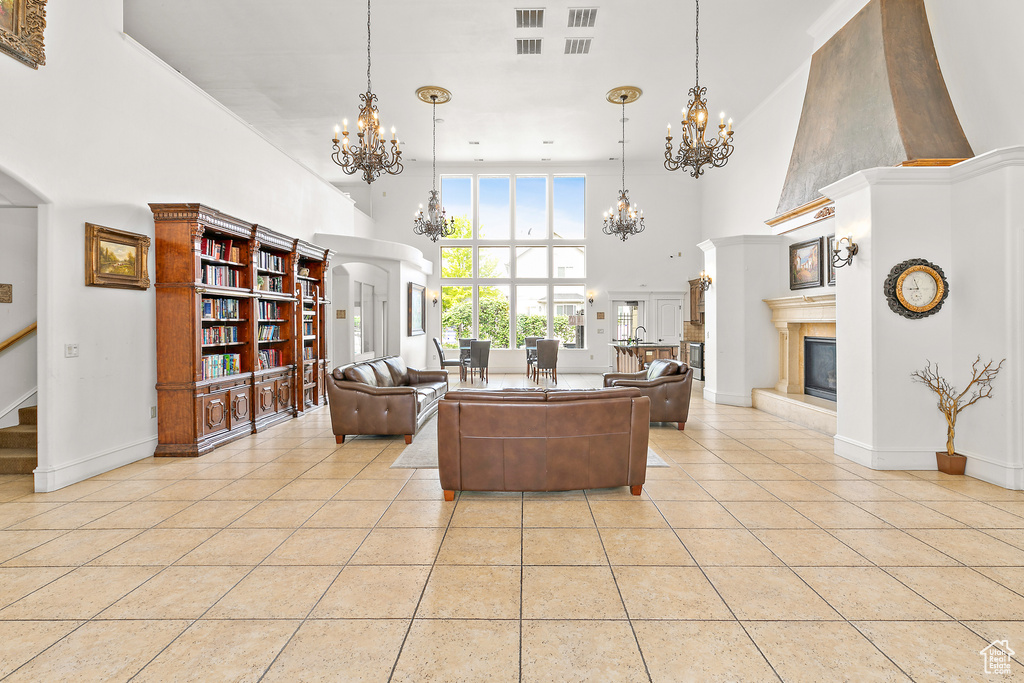 Living area featuring a chandelier, light tile patterned flooring, a towering ceiling, a large fireplace, and baseboards