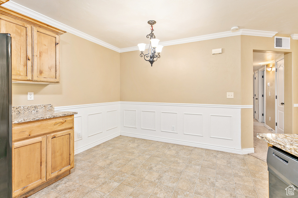 Unfurnished dining area with ornamental molding, a chandelier, and a wainscoted wall