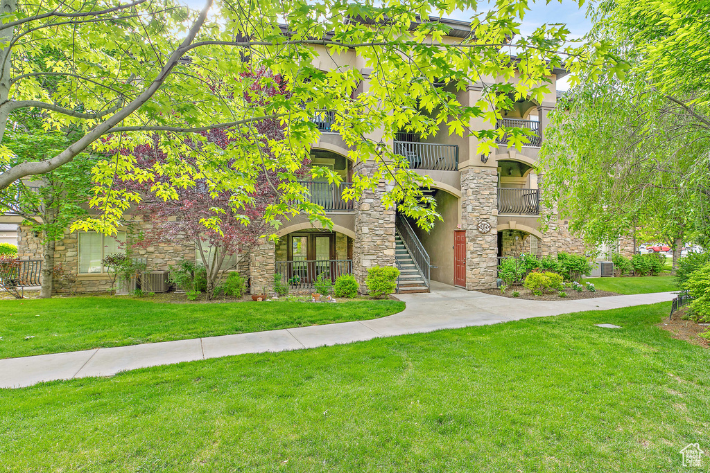 View of front of home featuring stone siding, central AC, a front lawn, and stucco siding