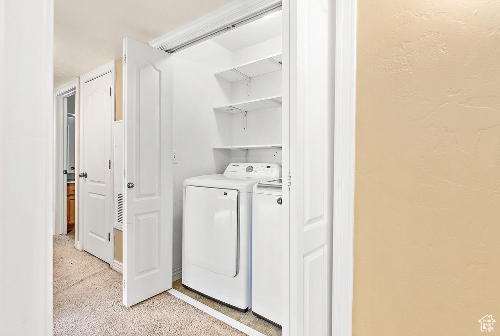 Laundry room featuring washer and dryer, light colored carpet, and a textured wall