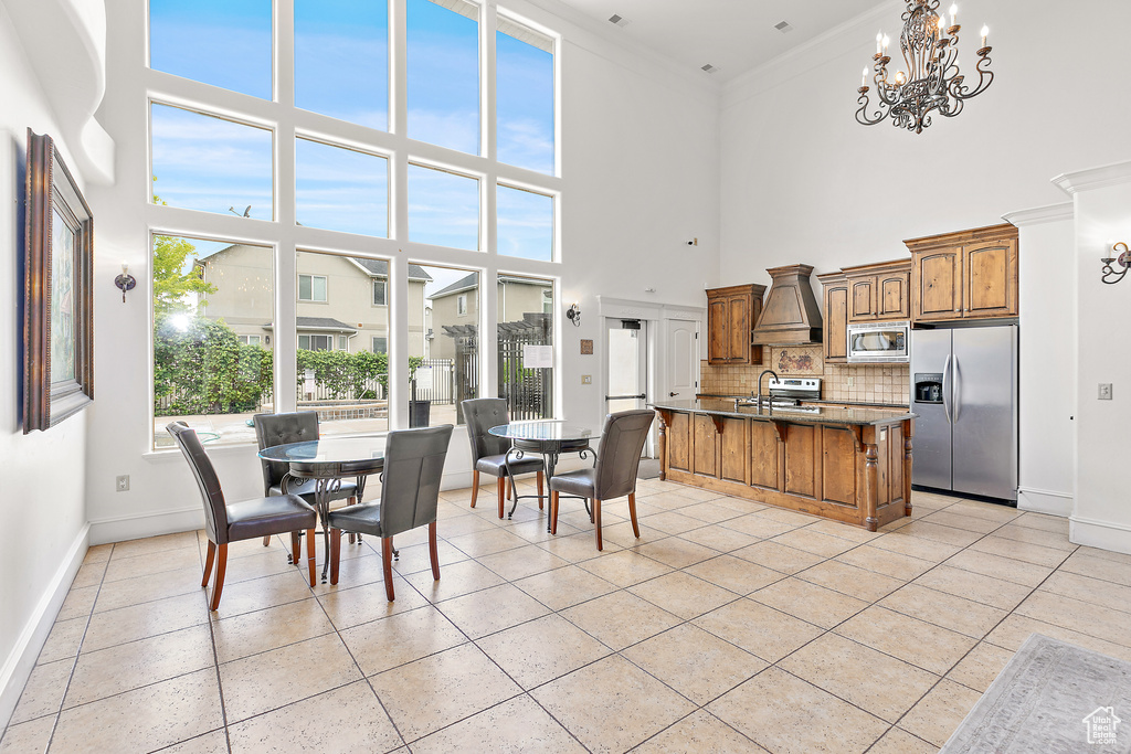 Dining space featuring light tile patterned floors, a high ceiling, baseboards, a chandelier, and crown molding