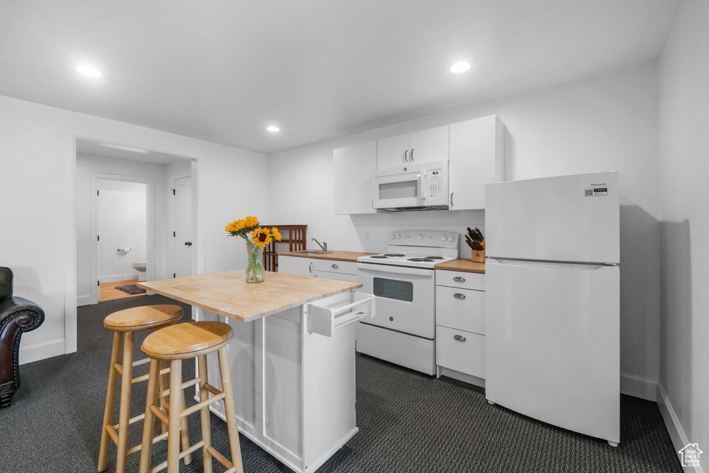 Kitchen featuring white appliances, wooden counters, dark carpet, white cabinetry, and recessed lighting
