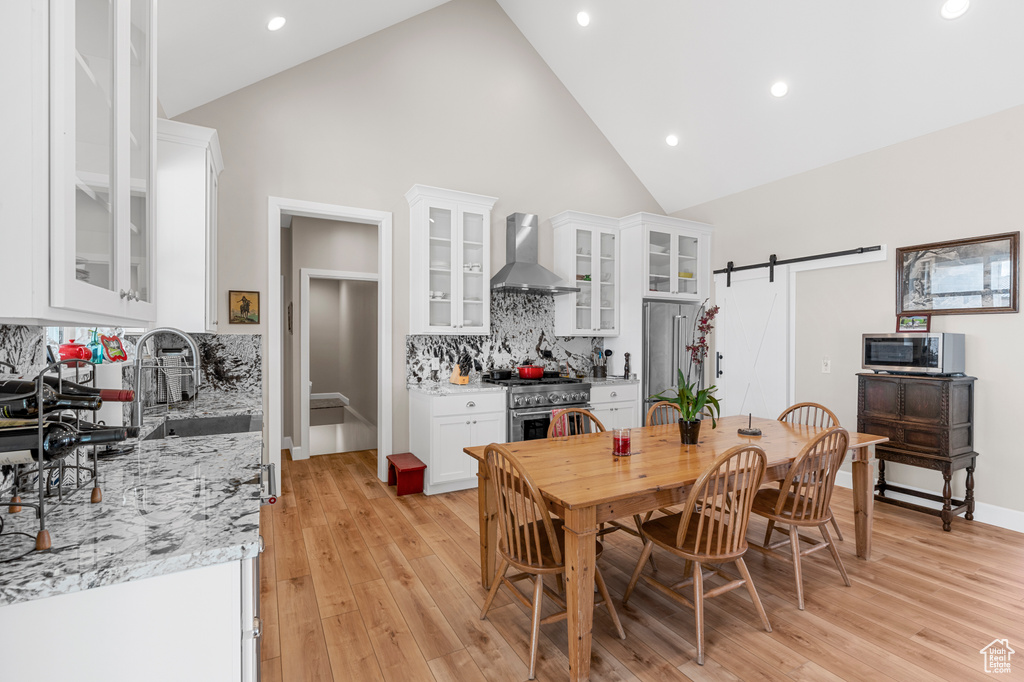 Dining area with a barn door, high vaulted ceiling, light wood finished floors, and recessed lighting