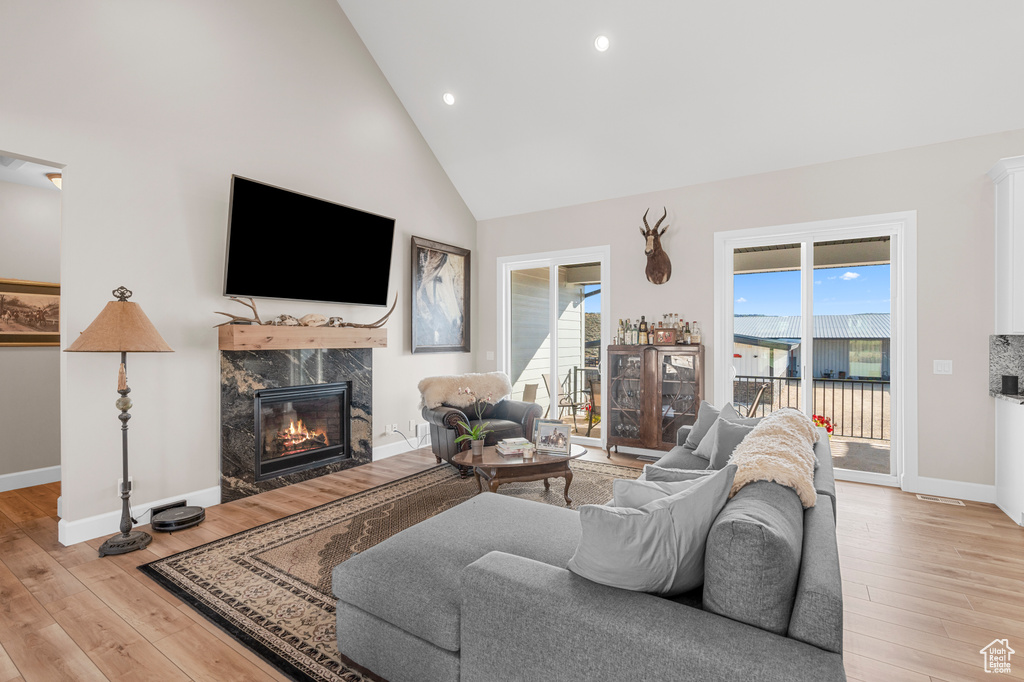 Living area featuring light wood-style flooring, high vaulted ceiling, a high end fireplace, baseboards, and recessed lighting