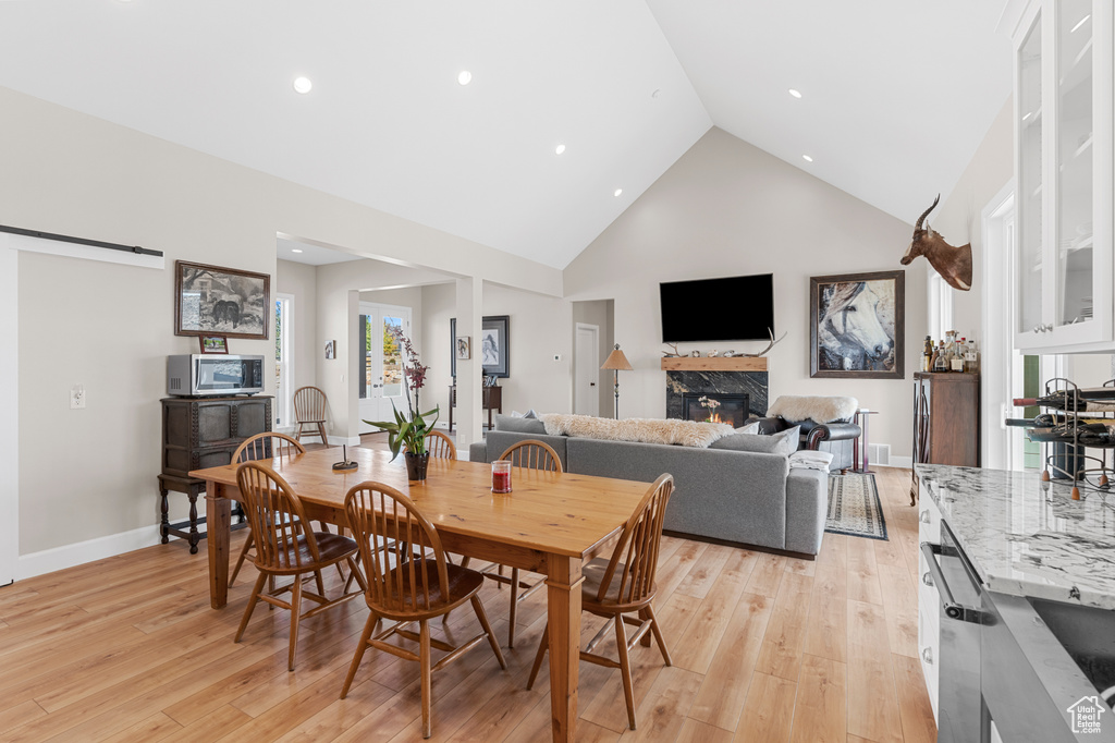 Dining room featuring high vaulted ceiling, light wood finished floors, a high end fireplace, recessed lighting, and baseboards