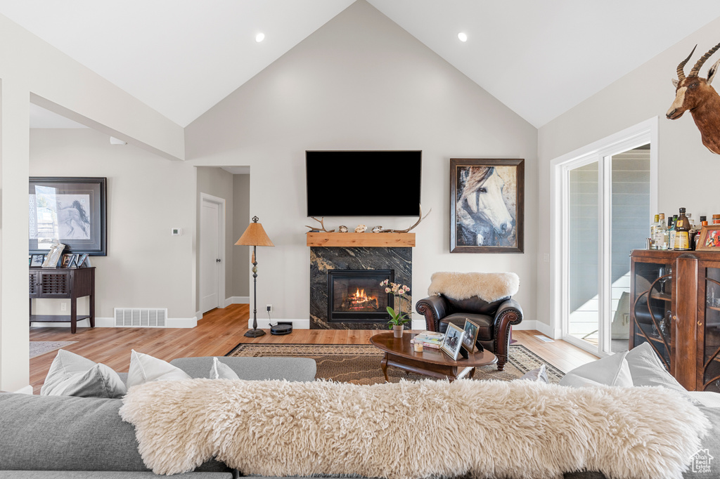 Living room featuring a high end fireplace, light wood-style flooring, high vaulted ceiling, baseboards, and recessed lighting