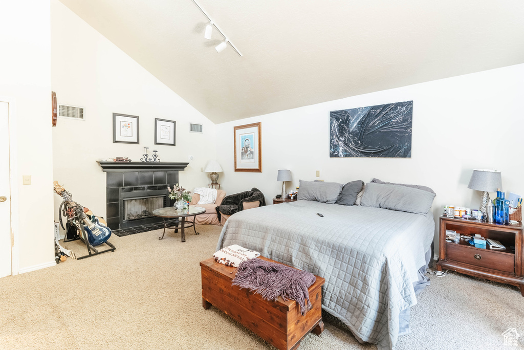 Carpeted bedroom featuring a fireplace, rail lighting, and lofted ceiling