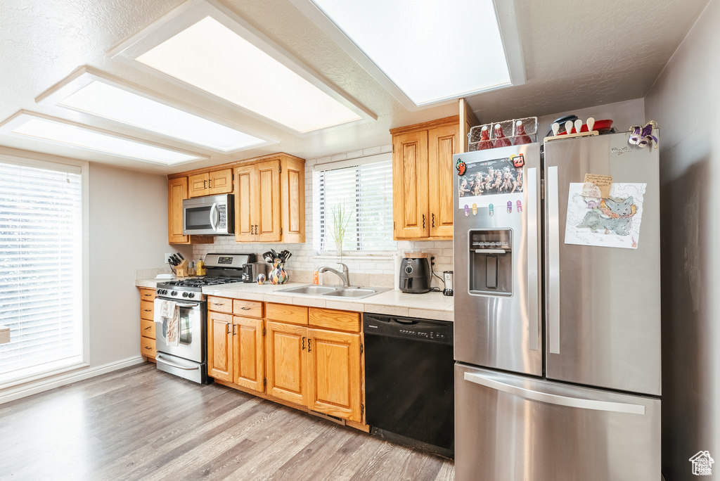 Kitchen with appliances with stainless steel finishes, a sink, tasteful backsplash, light countertops, and light wood-style floors