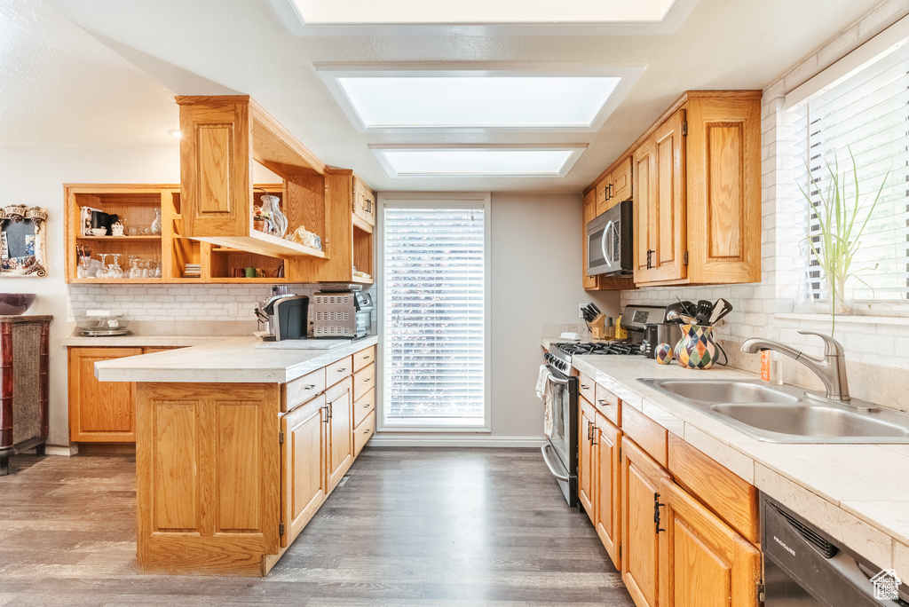 Kitchen featuring stainless steel appliances, a sink, open shelves, backsplash, and wood finished floors