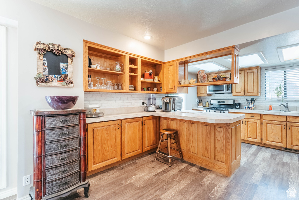 Kitchen featuring appliances with stainless steel finishes, a sink, light countertops, light wood-style floors, and tasteful backsplash