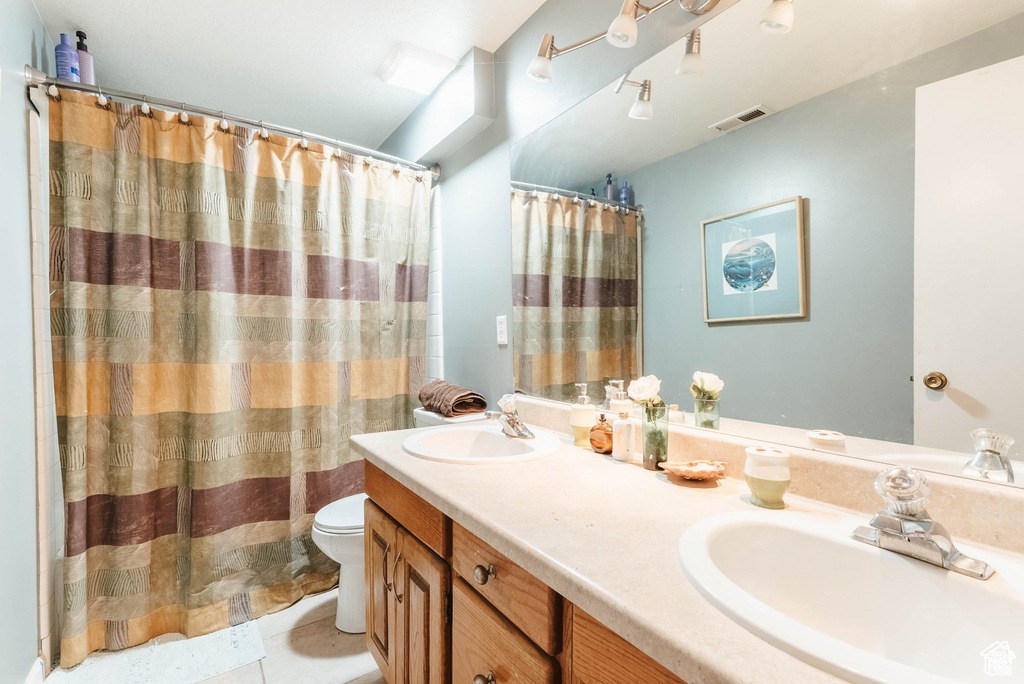 Full bath with toilet, double vanity, tile patterned flooring, and a shower with shower curtain