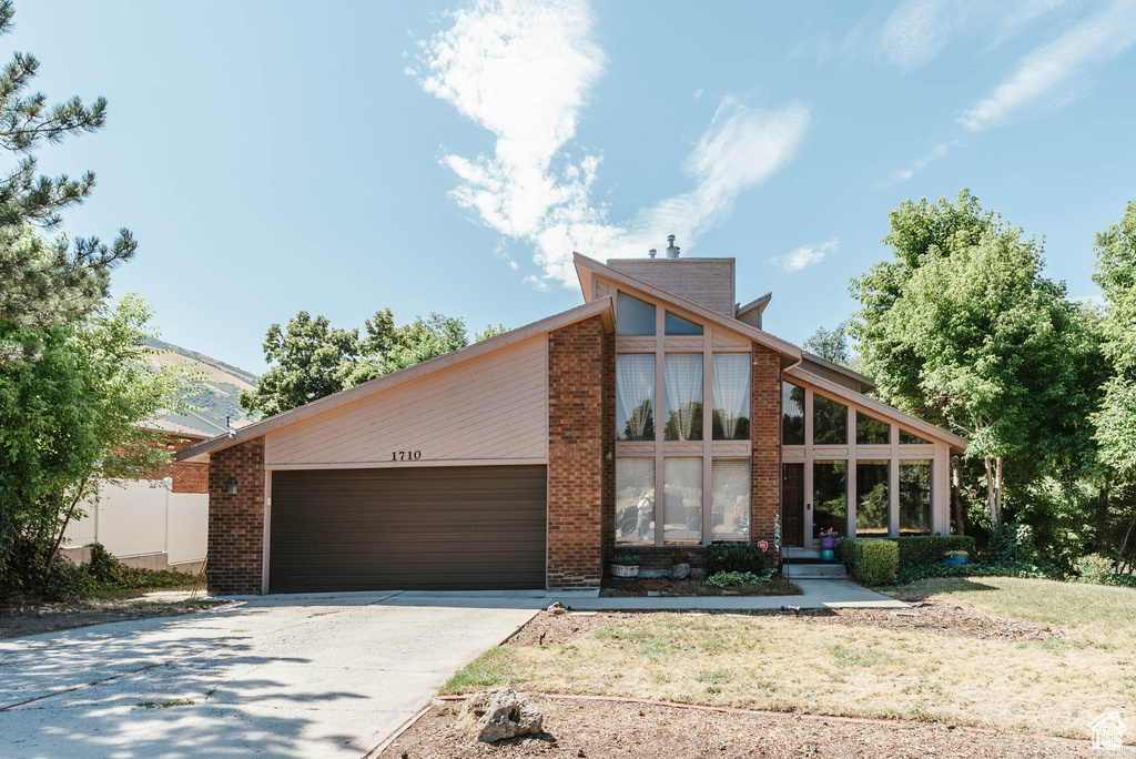 Mid-century modern home with an attached garage, concrete driveway, and brick siding