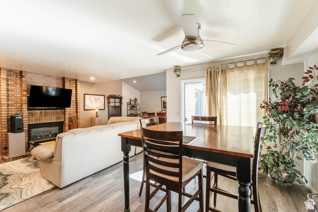Dining space featuring wood finished floors, ceiling fan, a brick fireplace, and recessed lighting
