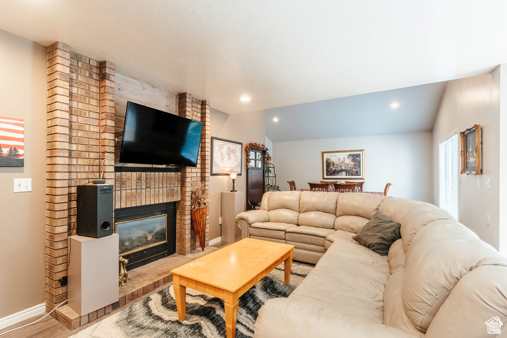Living area with wood finished floors, baseboards, vaulted ceiling, a brick fireplace, and recessed lighting