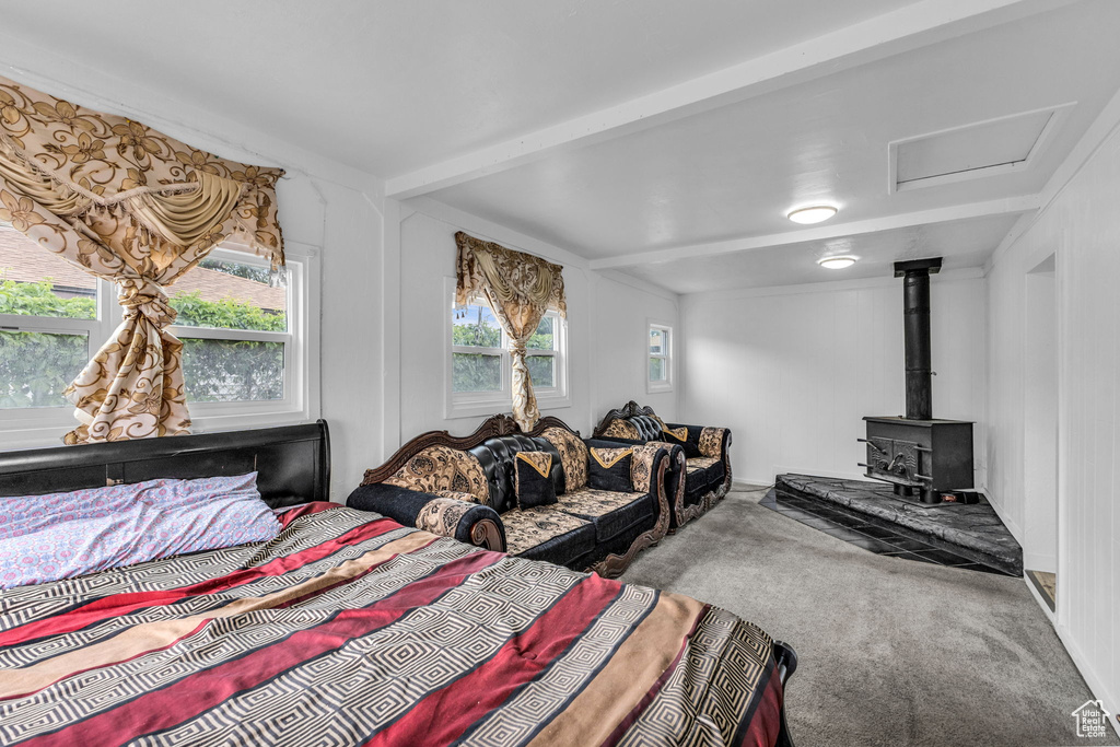 Bedroom with carpet flooring, a wood stove, beam ceiling, and attic access