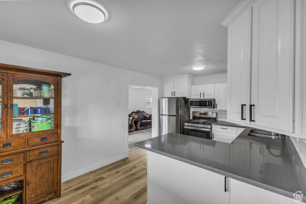 Kitchen with stainless steel appliances, light wood-type flooring, white cabinetry, a sink, and a peninsula