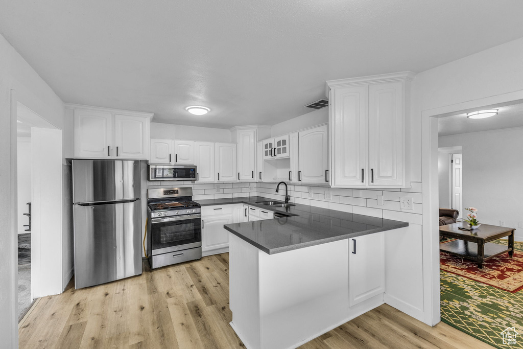 Kitchen featuring appliances with stainless steel finishes, dark countertops, a peninsula, a sink, and white cabinets