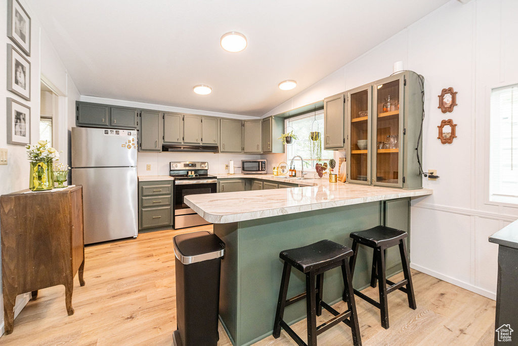 Kitchen featuring stainless steel appliances, a sink, a peninsula, light countertops, and light wood-style flooring