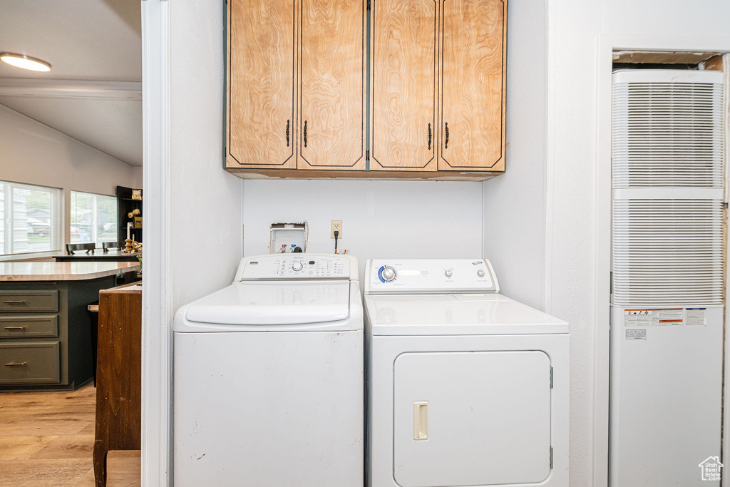 Laundry room featuring a heating unit, cabinet space, washing machine and dryer, and light wood-style flooring