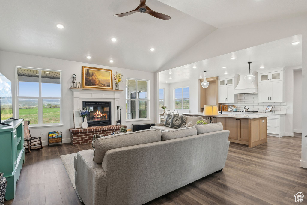 Living area with recessed lighting, a ceiling fan, a brick fireplace, lofted ceiling, and dark wood finished floors