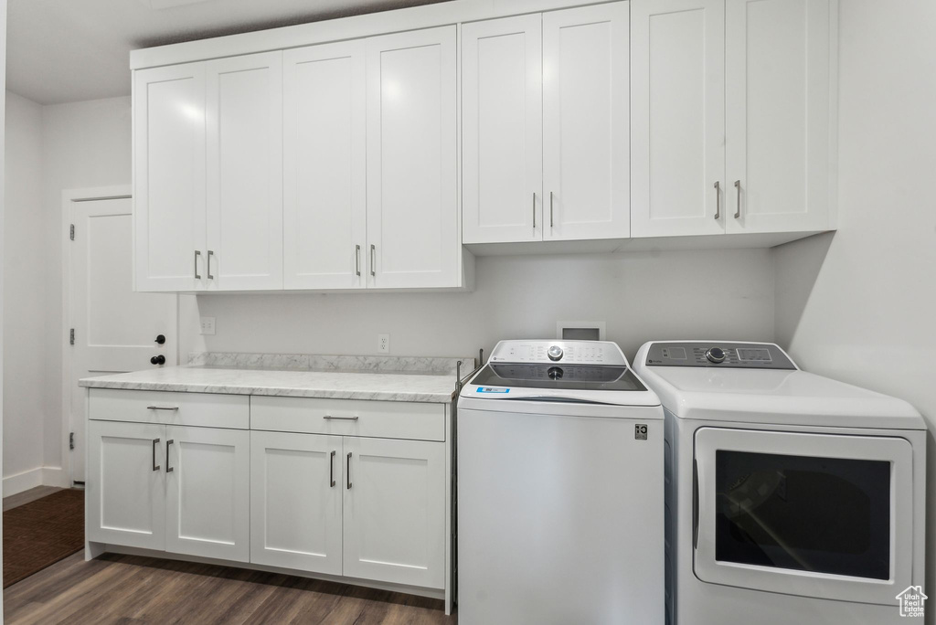 Washroom with washing machine and dryer, cabinet space, dark wood-type flooring, and baseboards