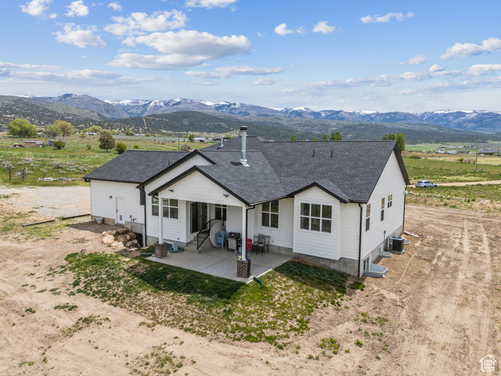 Back of property with a mountain view, a patio area, central AC unit, and roof with shingles