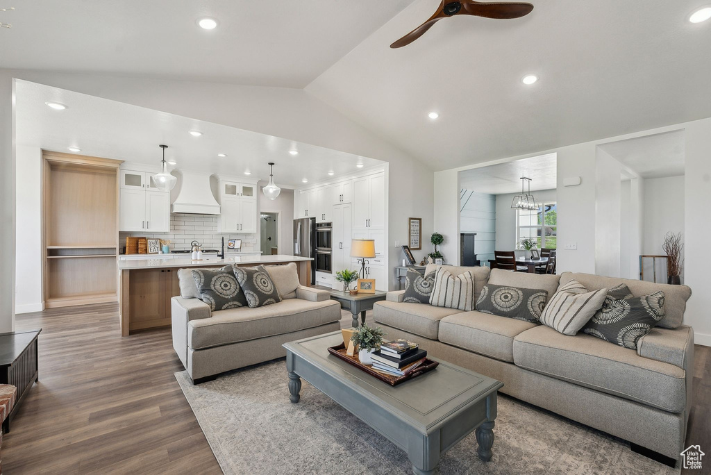 Living room featuring wood finished floors, lofted ceiling, a ceiling fan, a chandelier, and recessed lighting