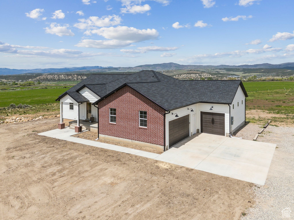 View of property exterior featuring driveway, a mountain view, an attached garage, roof with shingles, and brick siding
