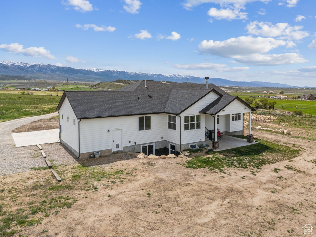 Rear view of house featuring a mountain view, gravel driveway, roof with shingles, and a patio area