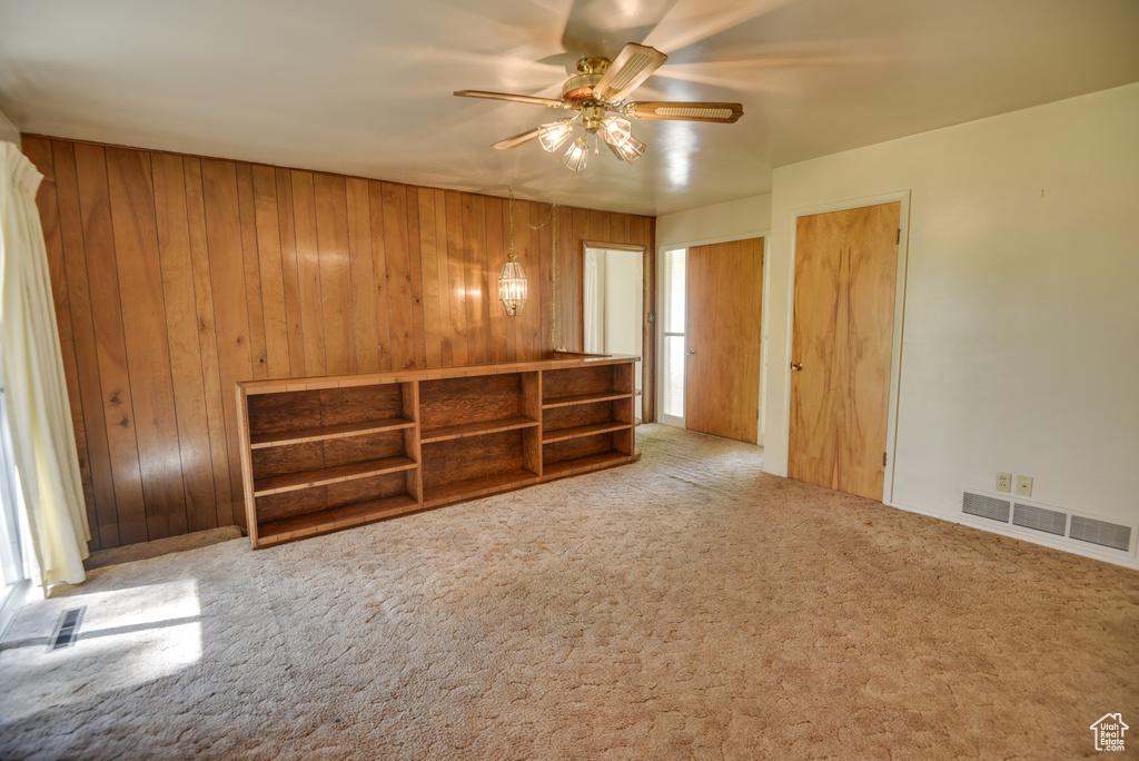 Unfurnished room featuring ceiling fan, wood walls, and carpet flooring