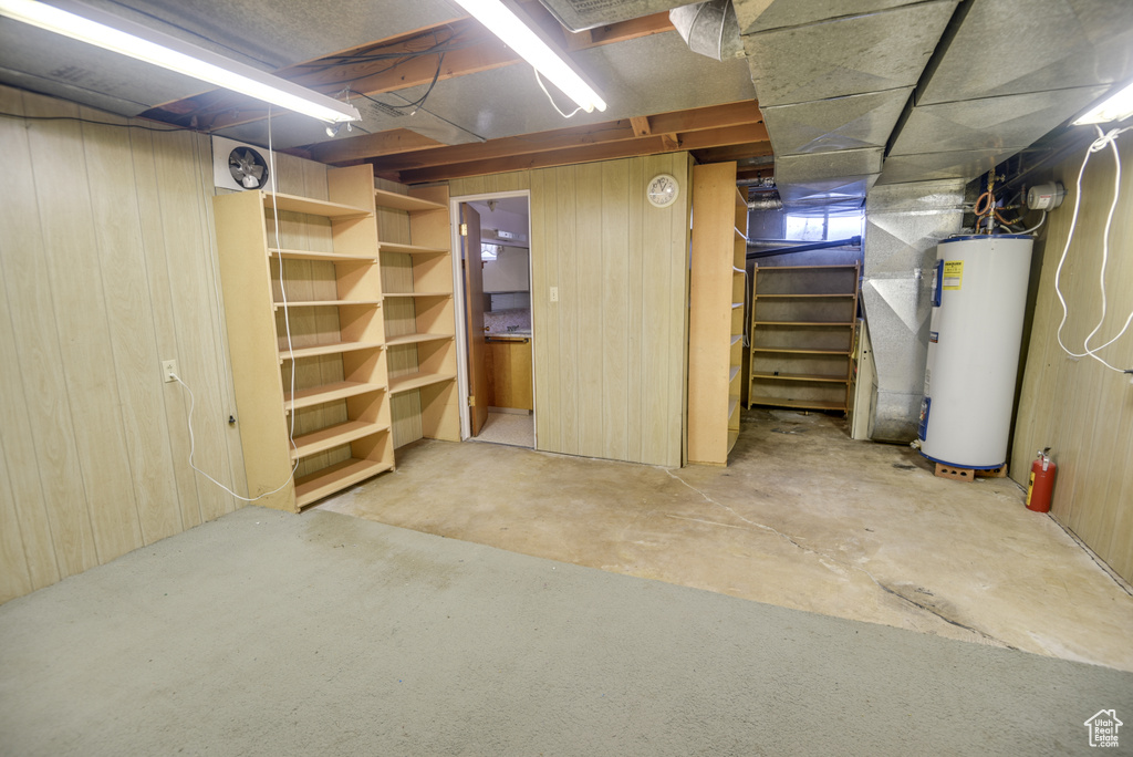 Unfinished below grade area with gas water heater, stairs, and wooden walls