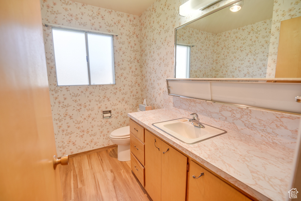 Bathroom featuring wood finished floors, wallpapered walls, toilet, vanity, and baseboards